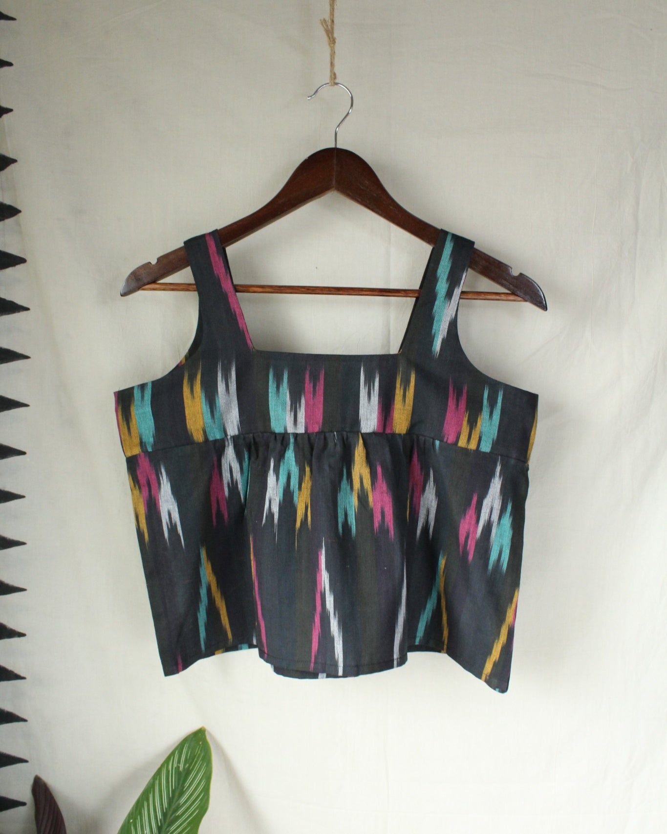 Black crop top with colorful geometric pattern on a hanger against a white background
