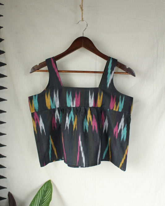 Black crop top with colorful geometric pattern on a hanger against a white background